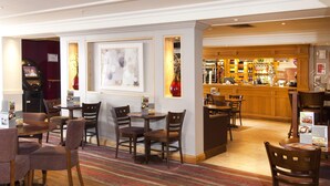 Vestíbulo de hotel con zona de bar, mesas y sillas para comer.