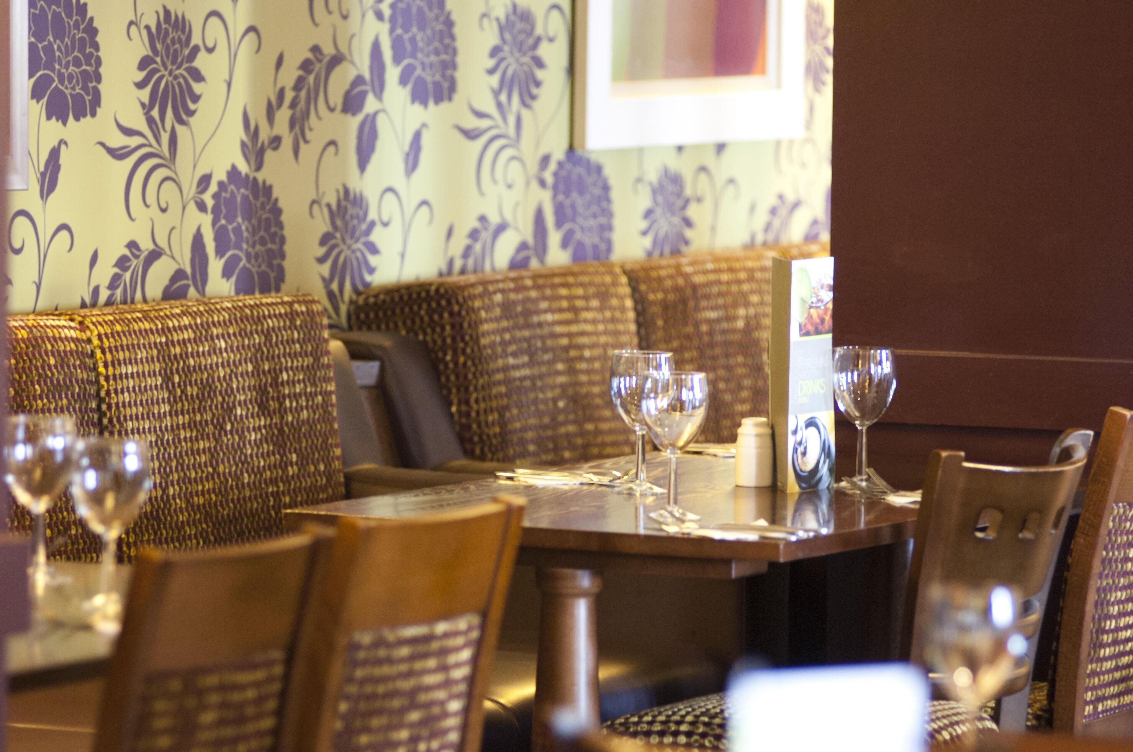 Interior de restaurante com mesa de madeira, assentos de vime e copos de vinho.
