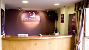 Un comptoir d’accueil d’hôtel avec une enseigne « Premier Inn », un emplacement pour les clés, un téléphone et une fenêtre avec des rideaux.