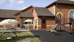 A brick building with a playground, picnic tables, and a covered seating area. - Premier Inn Thurrock East (Grays)
