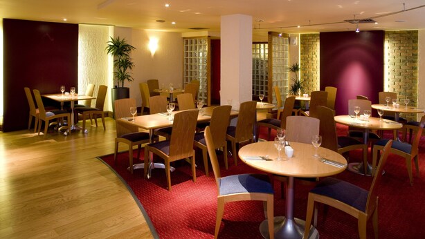 A restaurant with multiple tables and chairs, wooden flooring, and red carpeted areas. - Premier Inn London Kew Bridge (Brentford)