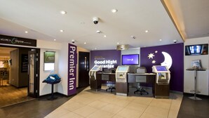 A hotel reception area with a check-in counter, a digital display, and a sign for the 'Premier Inn.' - Premier Inn London Edgware (Edgware)