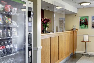 A reception area with a vending machine, a wooden reception desk, and a small table with a sign.