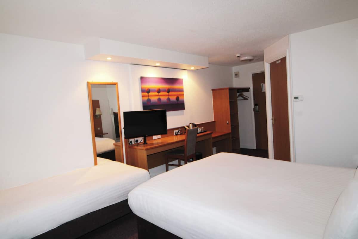 Une chambre d’hôtel avec deux lits simples, un bureau avec une chaise, une télévision et un tableau au mur.