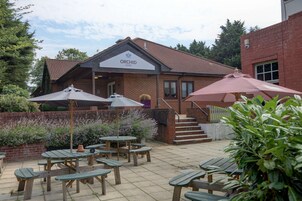 An Orchid Hotel with a brick exterior, outdoor seating area with tables and umbrellas, and a staircase leading to the entrance.