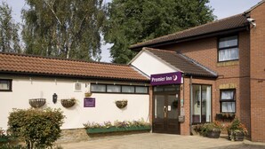 A brick building with a sign for 'Premier Inn' and a tiled roof. There are flower planters along the front and a small tree in the foreground. - Premier Inn London Romford West (Romford)