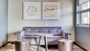 Una habitación moderna con un sofá gris, dos otomanas, una mesita redonda y dos cuadros decorativos con mensajes inspiradores.