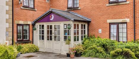 A brick building with a conservatory, a gated entrance, and potted plants.