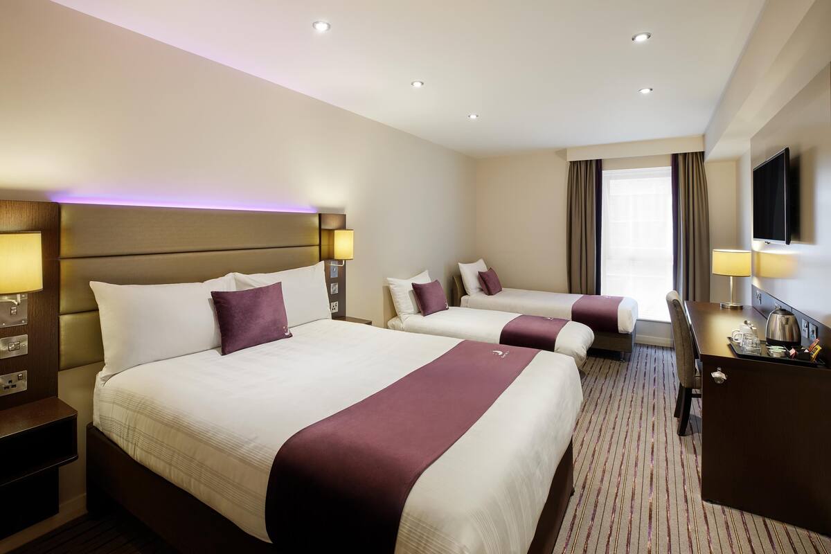 A hotel room with two beds, a desk with a television, and a window with curtains.