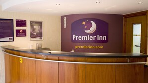 Egy ívelt pulttal rendelkező szállodai recepció, rajta a „Premier Inn” felirattal, és a falon több tájékoztató plakát.
