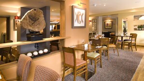 A hotel lobby with a reception desk, wooden chairs, a patterned rug, and a large abstract painting on the wall. - Premier Inn Brentwood (Brentwood)