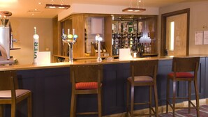 A bar area with wooden stools, a bar counter, and a variety of bottles. - Premier Inn Brentwood (Brentwood)