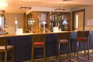 Zona de bar con taburetes de madera, mostrador y una variedad de botellas.