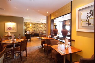 Un restaurante con varias mesas y sillas, un muro con diseño y un jarrón grande a la derecha.