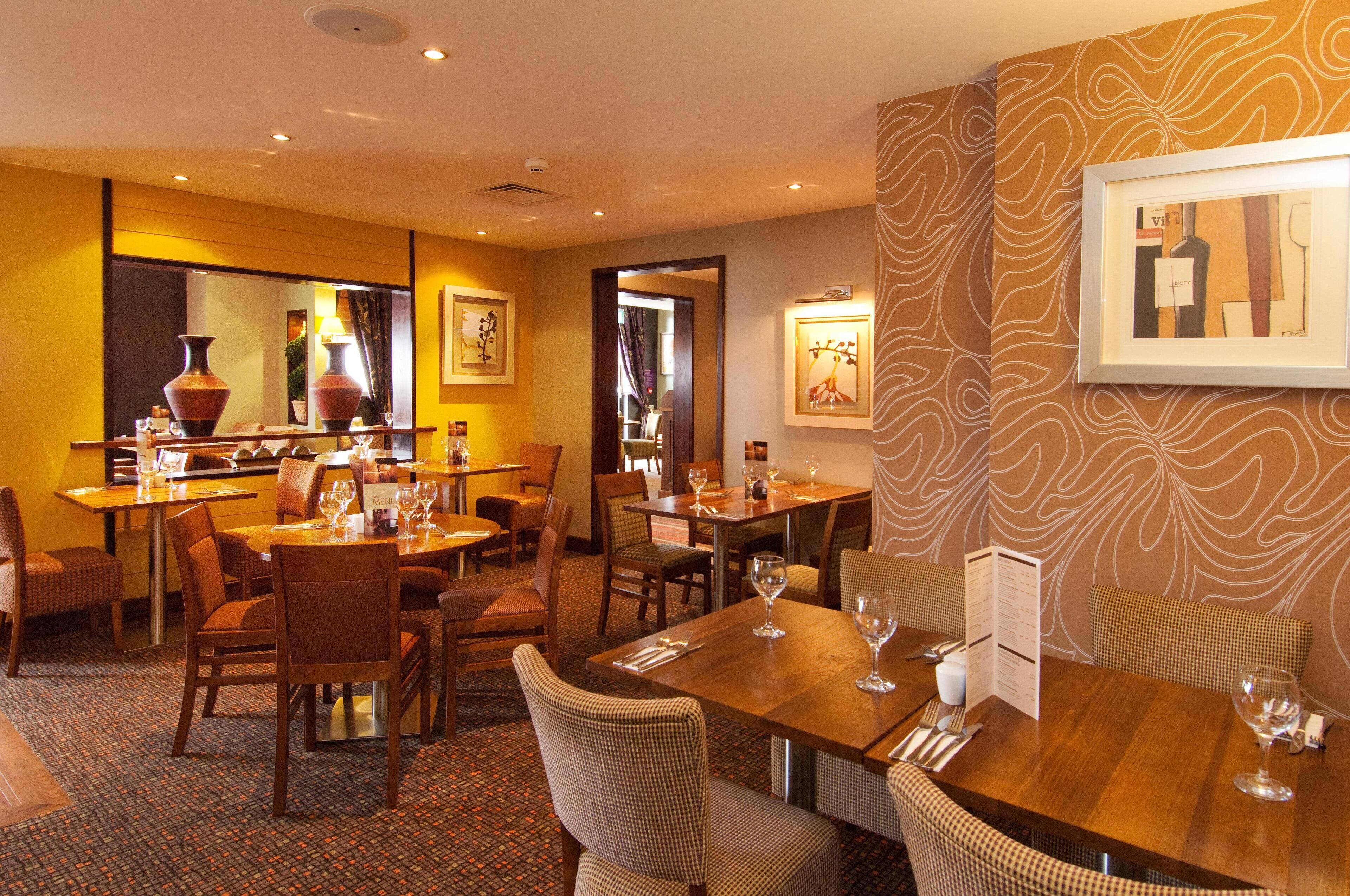 A hotel dining area with multiple tables and chairs, a patterned wall, and framed artwork.