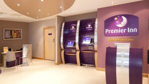 Een receptiegebied van Premier Inn met een incheckbalie, zelfservicekiosken en een 'Welcome'-bord.