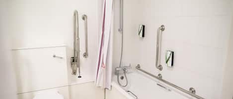 Une salle de bain équipée de toilettes, d’une douche avec des barres d’appui et d’une baignoire avec un pommeau de douche amovible.