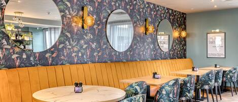 L’intérieur d’un restaurant avec des tables rondes, des murs ornés de motifs floraux et un banc en bois.
