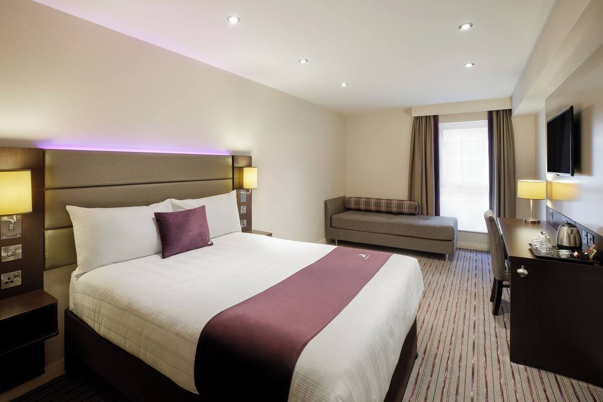 A hotel room with a large bed, a desk, a sofa, and a TV.