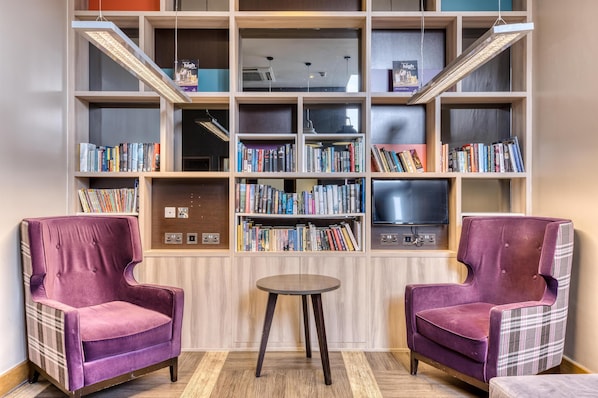 A room with two purple armchairs, a small round table, and a bookshelf filled with books. - Premier Inn London Southwark Tate Modern (London)