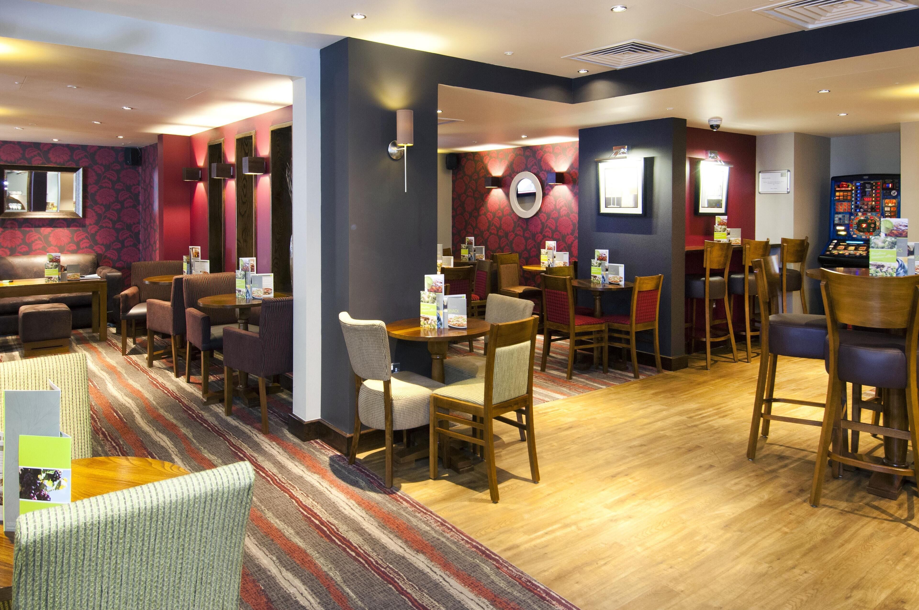 A hotel lobby with multiple seating areas, including a bar and a dining area with tables and chairs.