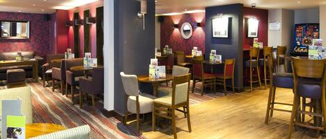 A hotel lobby with multiple seating areas, including a bar and a dining area with tables and chairs.