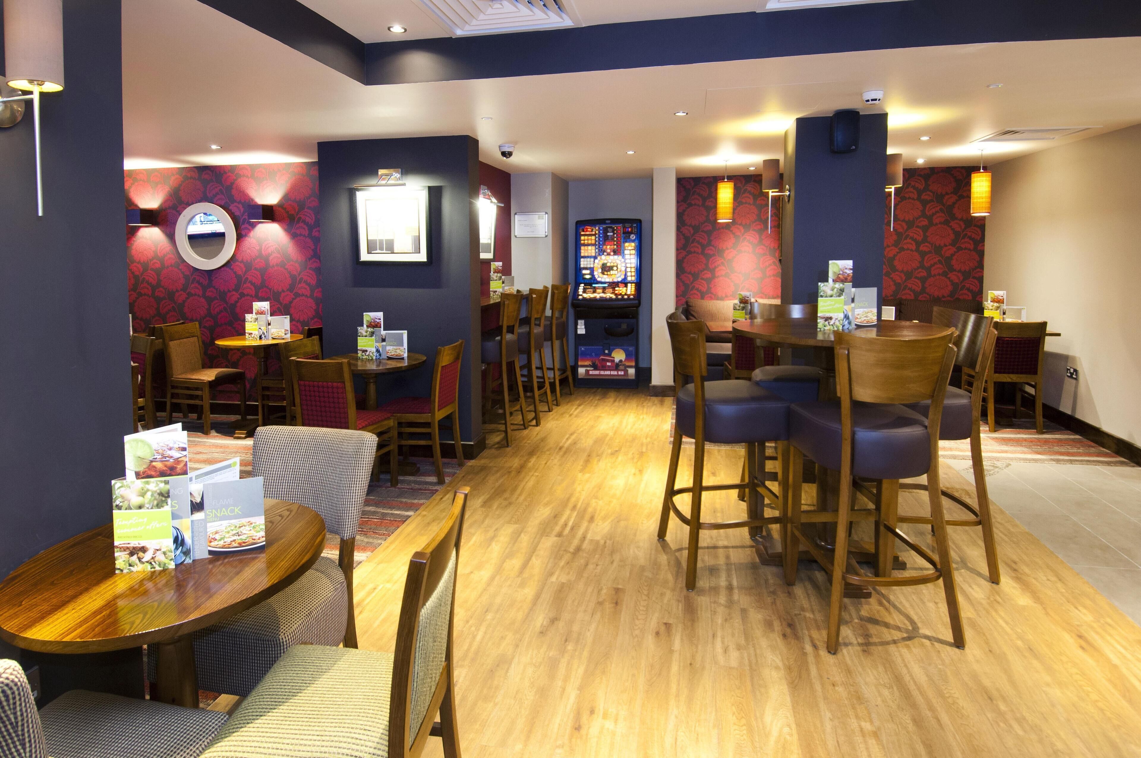 A restaurant with wooden tables and chairs, a patterned wall, and a menu stand.