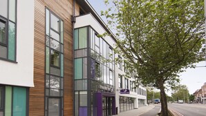 Een modern gebouw met grote ramen, een trottoir met bomen en een fietspad.