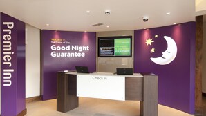 A check-in counter with a 'Premier Inn' sign, a digital screen displaying local news, and a wall with a crescent moon and stars. - Premier Inn London Dagenham (Dagenham)