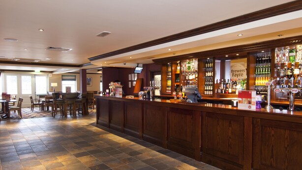 A bar area with a counter, seating, and a sign reading 'Brewers Fayre.' - Premier Inn London Dagenham (Dagenham)
