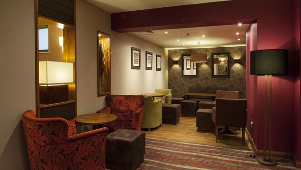 Een hotel lobby met zitplaatsen, een receptiebalie, ingelijste foto’s aan de muur en een lamp.