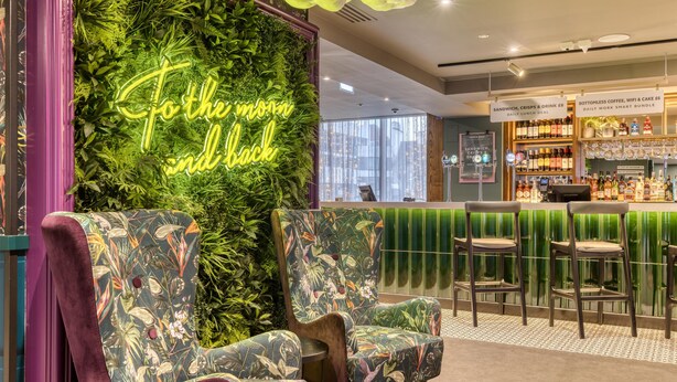 Eine Bar mit Neonreklame, Barhocker und einer grünen Wand mit Pflanzen.