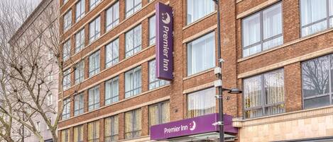 Un hotel de varios pisos con un llamativo letrero de 'Premier Inn', grandes ventanales y un escaparate visible con toldo azul.