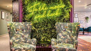 Ein Zimmer mit zwei blumigen Sesseln, einem kleinen runden Tisch und einer vertikalen Gartenwand mit einem Neon-Schild mit der Aufschrift 'To the moon and back'.