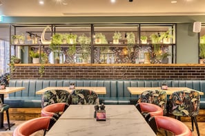 Un restaurant avec des banquettes, des tables et un mur recouvert de plantes en pot.