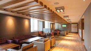 A modern interior with a long wooden ceiling, seating areas, a TV screen, and a dining area. - Premier Inn London Hendon - The Hyde (London)