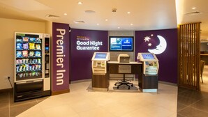 A hotel lobby with a vending machine, a check-in counter, and a wall sign reading 'Premier Inn Good Night Guarantee'. - Premier Inn London Hendon - The Hyde (London)