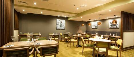 A restaurant with multiple tables and chairs, ceiling lights, and wall-mounted pictures.