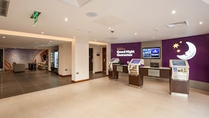 En hotellobby med en skylt som utlovar ”garanterat god natts sömn”, en digital skärm, en incheckningsdisk och en självbetjäningskiosk.