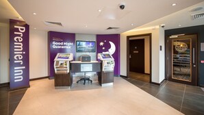 Un espace d’accueil d’hôtel comprenant un kiosque numérique, un écran d’ordinateur et un panneau indiquant « Premier Inn ».