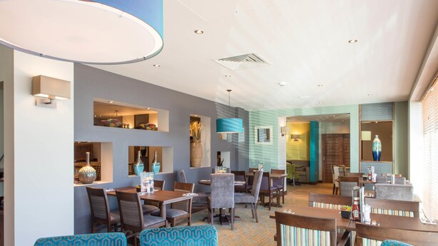 A restaurant with multiple dining areas, including a bar and a seating area with patterned chairs. - Premier Inn London Edmonton (London)