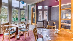 Un espace repas avec des tables et des chaises, des panneaux indiquant les issues de secours et de grandes fenêtres donnant sur des bâtiments.