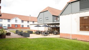 A courtyard with outdoor seating, potted plants, and a building with a red-tiled roof. - Premier Inn Liverpool North (Bootle)