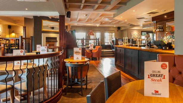 A restaurant with a bar area, seating with tables and chairs, and a sign indicating a special offer for grilling great steak. - Premier Inn Liverpool North (Bootle)