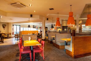 Een restaurant met zitjes, tafels en oranje hanglampen.