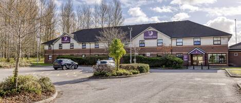 A Premier Inn hotel with a parking lot, a car, and a clear sky.