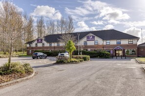 A Premier Inn hotel with a parking lot, a car, and a clear sky. - Premier Inn Liverpool - Tarbock (Liverpool)