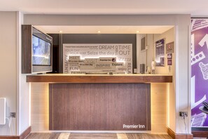 A hotel reception desk with a large welcome sign, a television, and a wall with various posters.