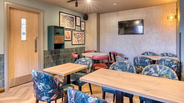 Un restaurante con mesas y sillas de madera, un televisor montado en la pared y cuadros enmarcados.