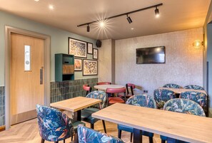 A restaurant with wooden tables and chairs, a TV mounted on the wall, and framed artwork on the wall.